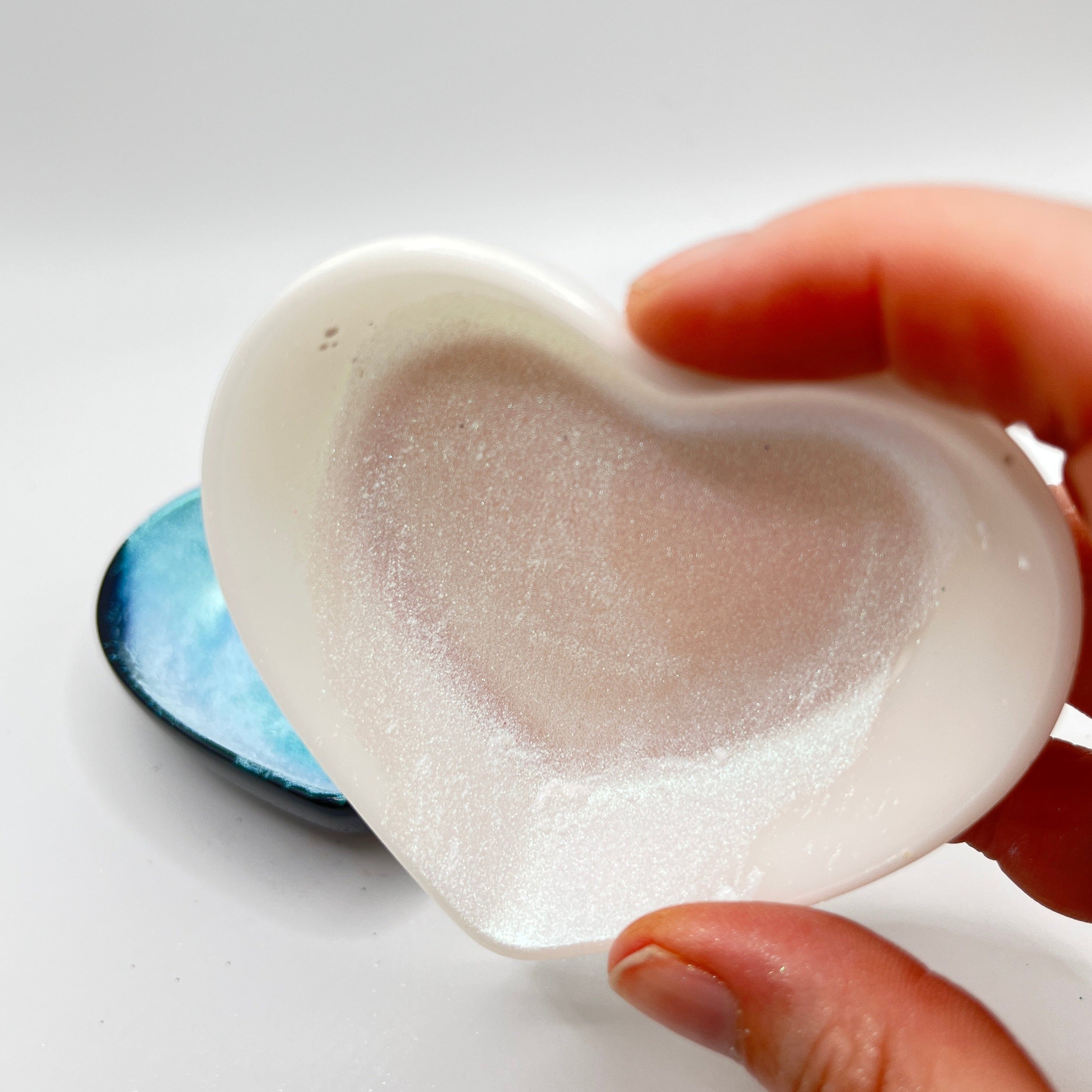 Fingers holding a white heart shaped dish with a white chameleon mica powder.