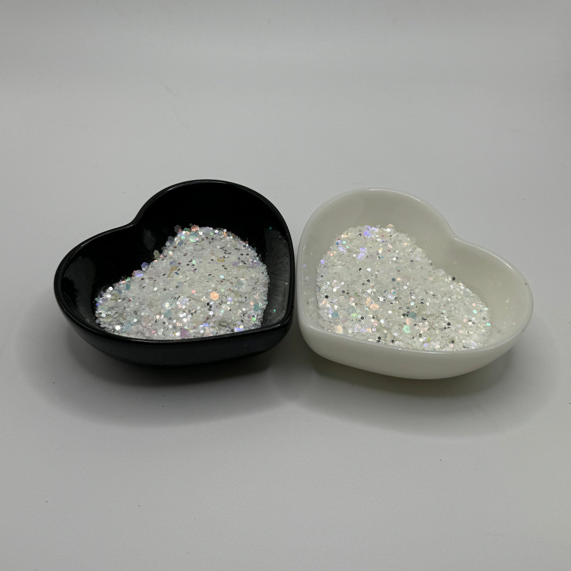 Two heart-shaped containers of glitter, one black and the other white, both showing a chunky white glitter mix