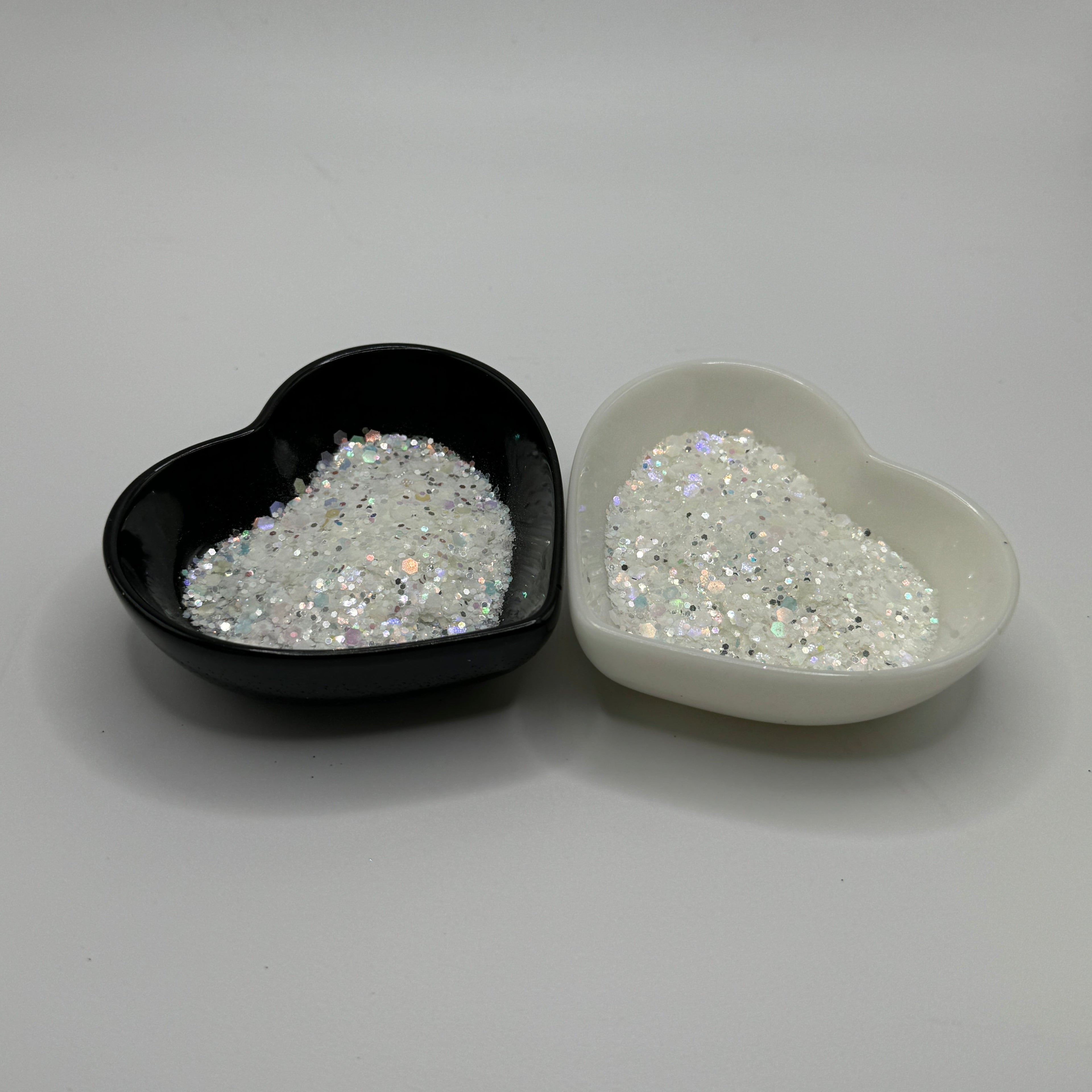 Two heart-shaped containers of glitter, one black and the other white, both showing a chunky white glitter mix