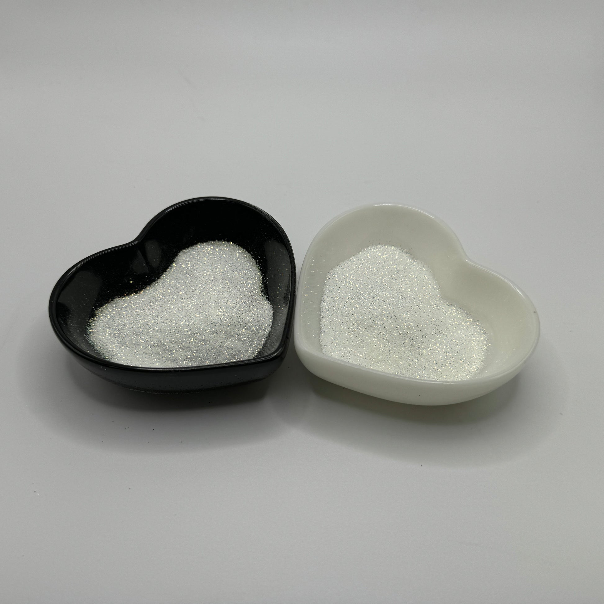Two heart-shaped containers of glitter, one black and the other white, both showing an extra fine, white glitter