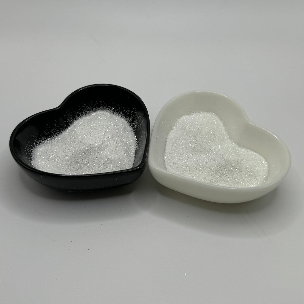 Two heart-shaped containers of glitter, one black and the other white, both showing an extra fine, white glitter.