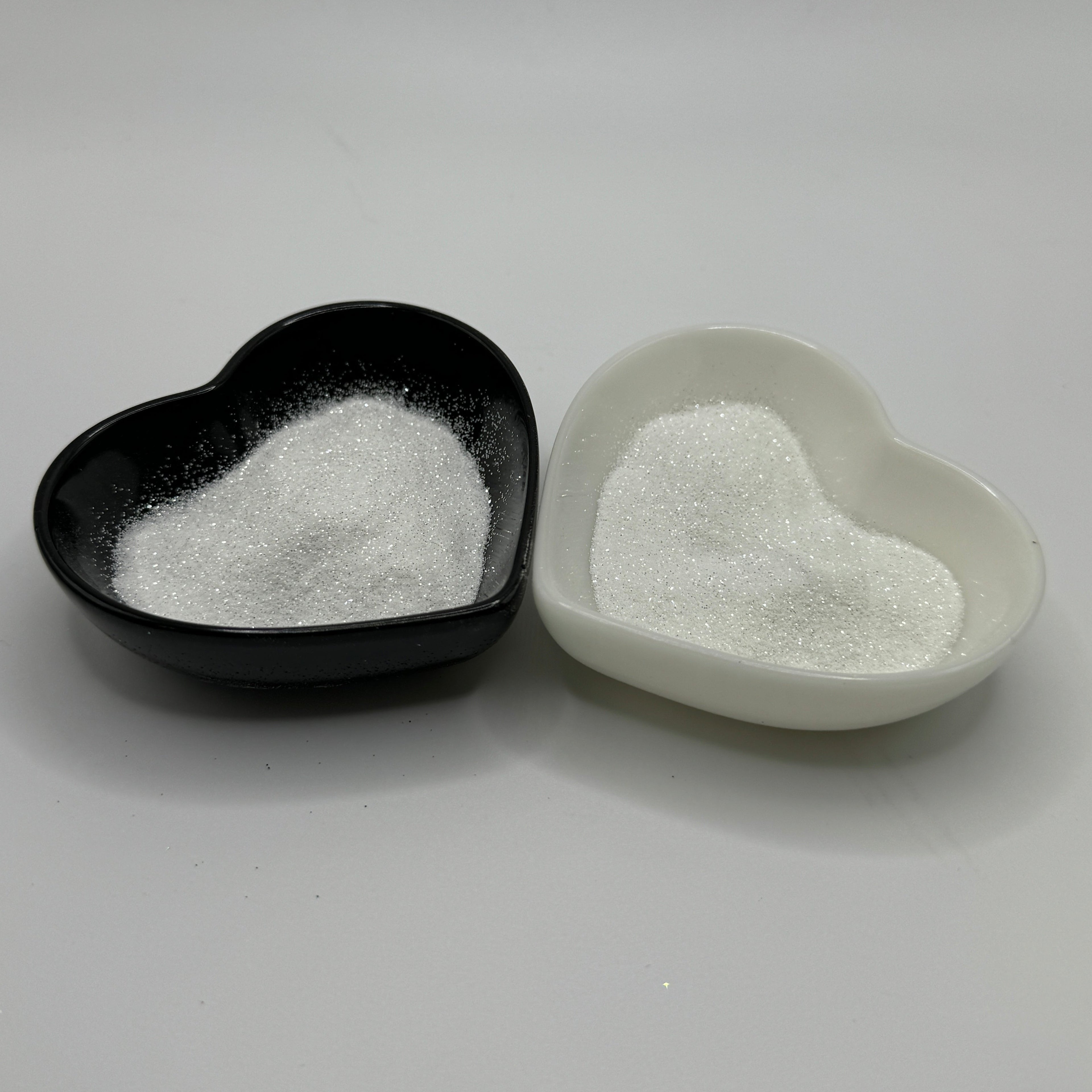 Two heart-shaped containers of glitter, one black and the other white, both showing an extra fine, white glitter.