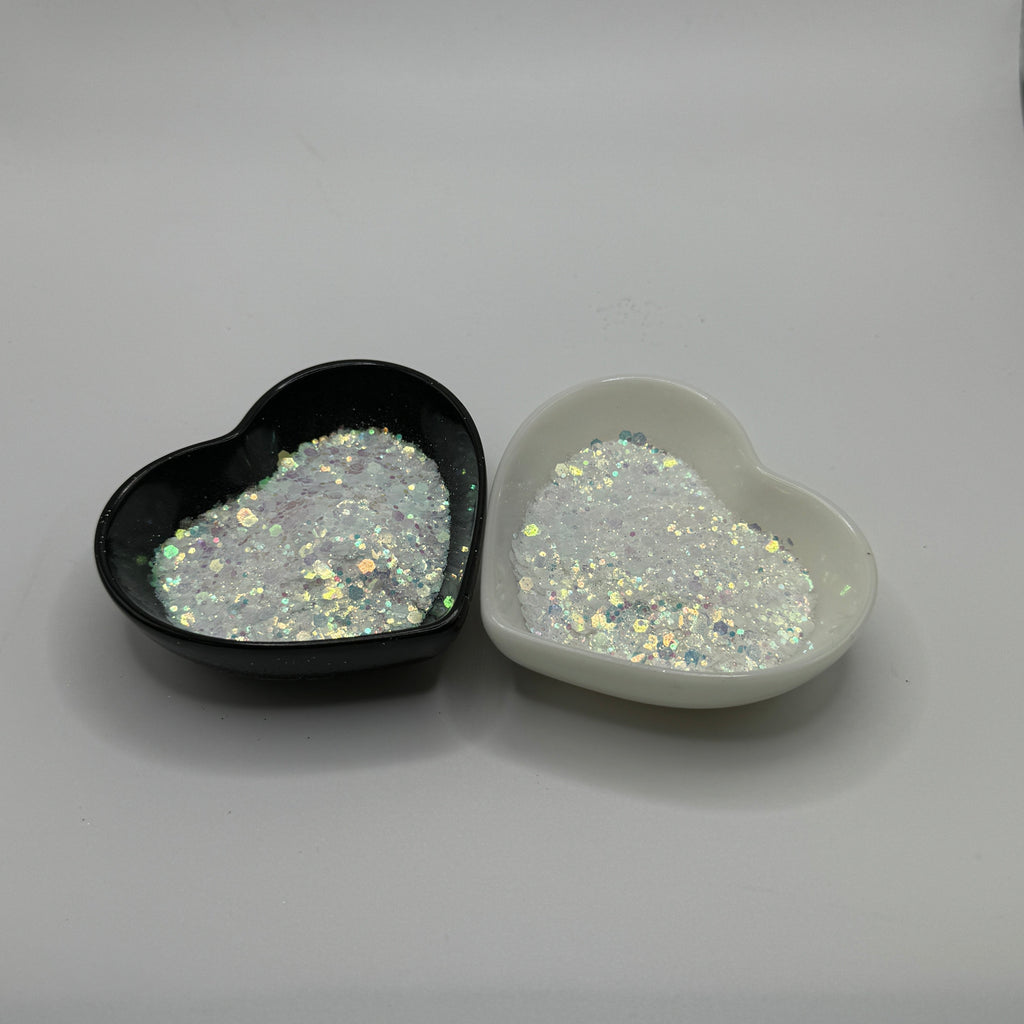 Two heart-shaped containers of glitter, one black and the other white, both showing a chunky, white glitter mix