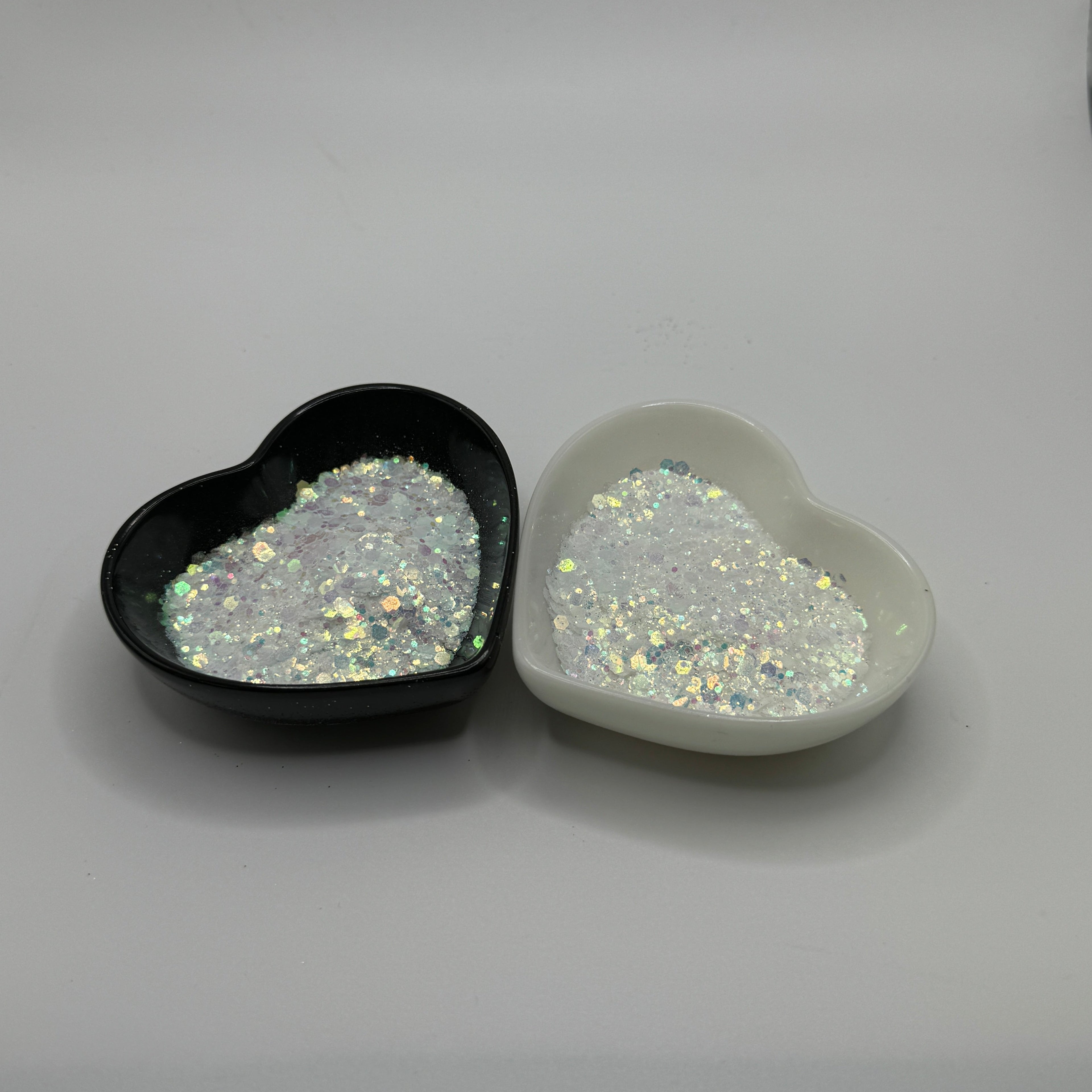 Two heart-shaped containers of glitter, one black and the other white, both showing a chunky, white glitter mix