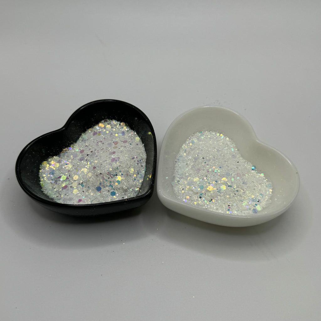 Two heart-shaped containers of glitter, one black and the other white, both showing a chunky white glitter mix