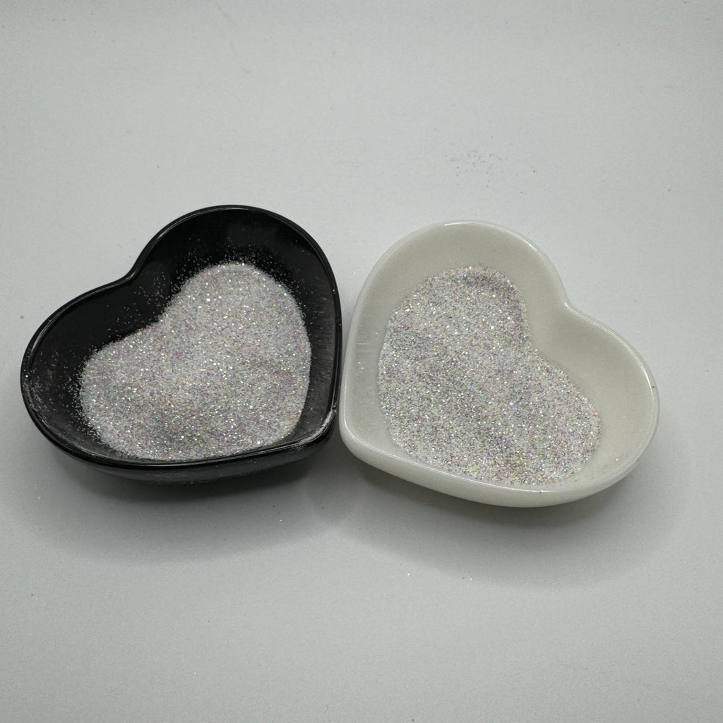Two heart-shaped containers of glitter, one black and the other white, both showing an extra fine, white rainbow glitter mix