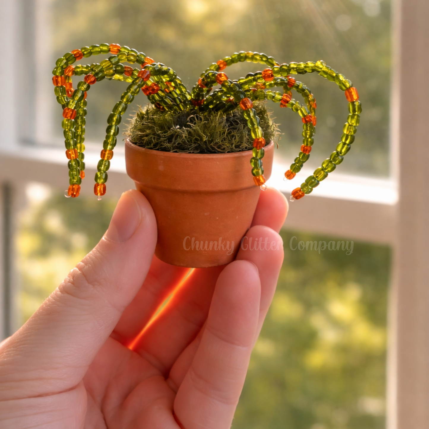 Hand holding a small potted plant made of beads.