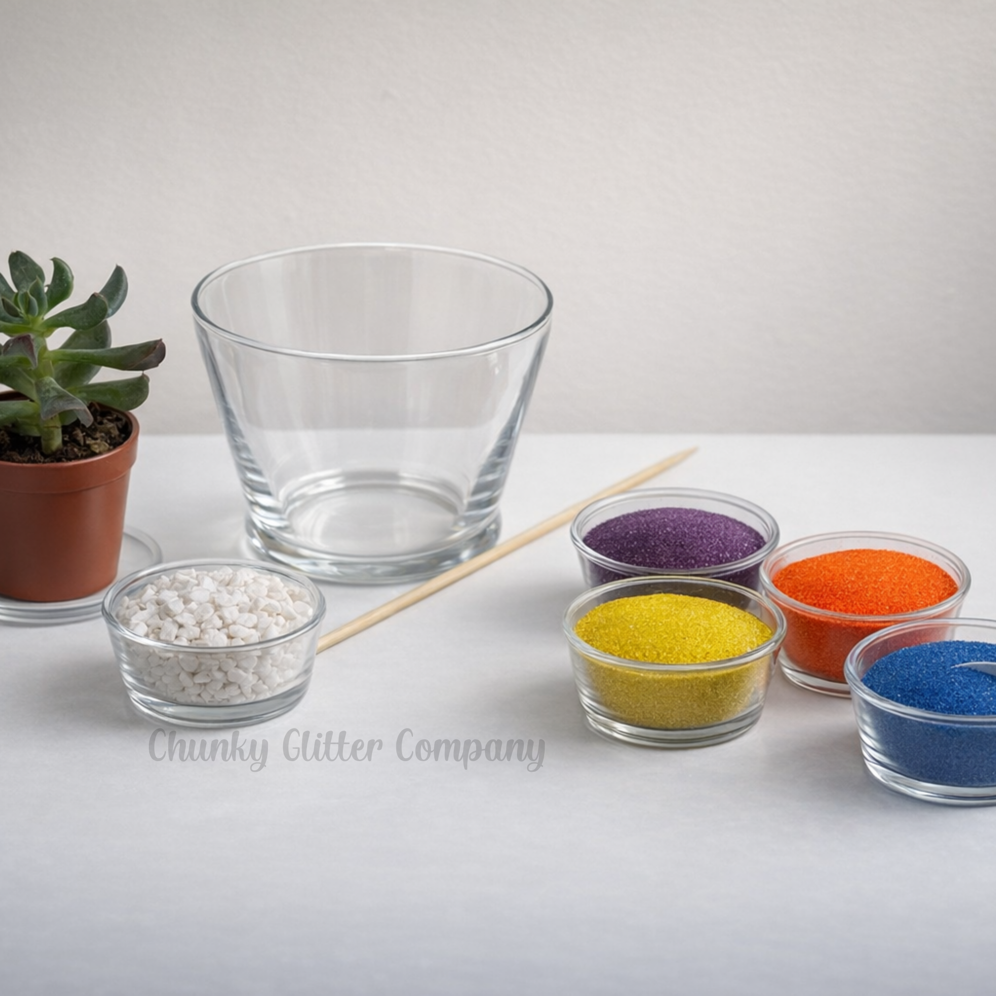Clear glass vase with colorful sand and a plant on a light surface