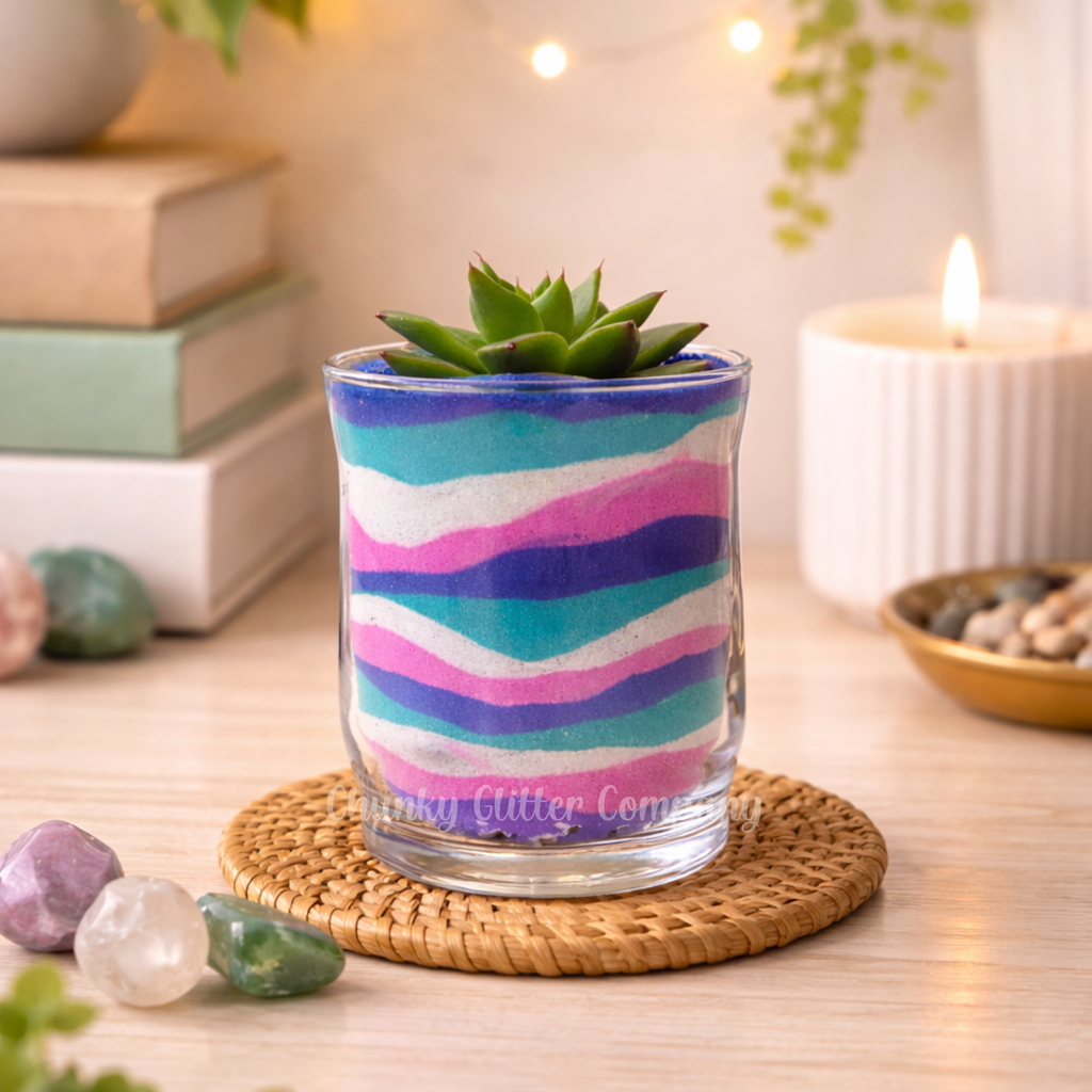 Colorful sand art glass with a succulent on a wooden table with books and a candle in the background