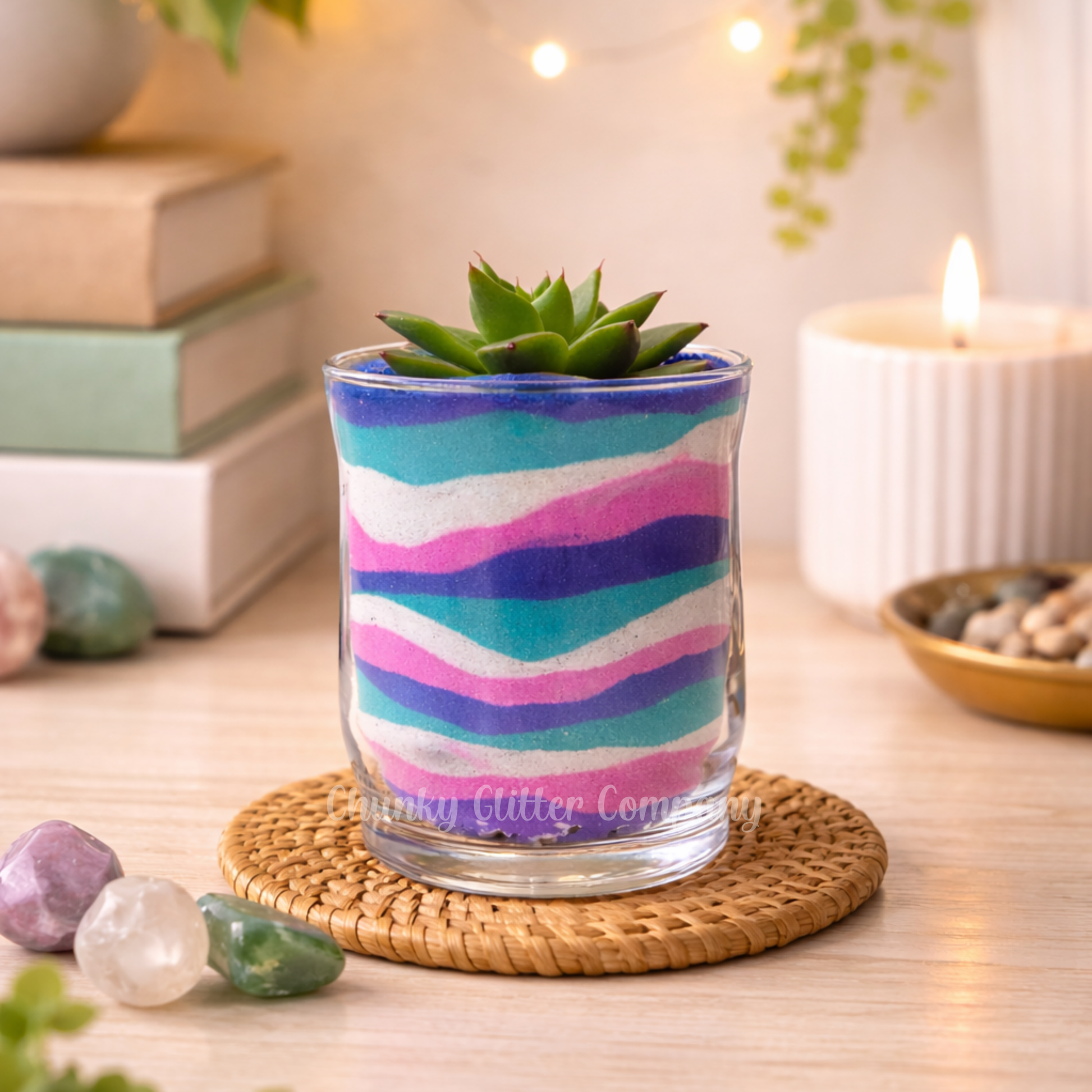Colorful sand art glass with a succulent on a wooden table with books and a candle in the background