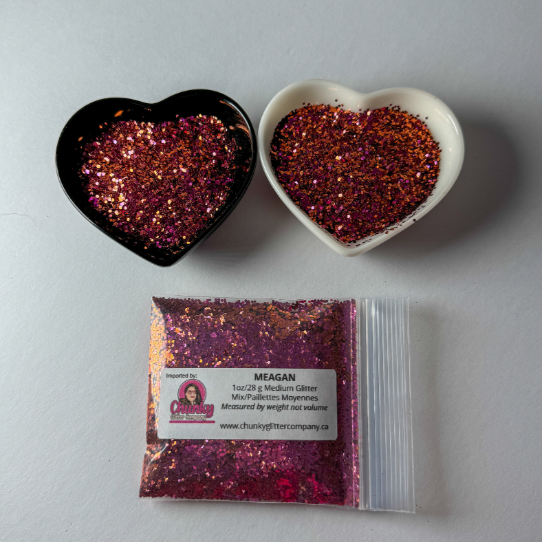 Two heart-shaped containers of glitter, one black and the other white, both showing a medium glitter, multicolored glitter mix and a bag of glitter with a label that reads Meagan.