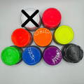 Nine small round plastic tubs with colorful lids arranged in a pyramid on a light gray background. The top-left tub is crossed out with a large black X, indicating it is excluded from the color selection.