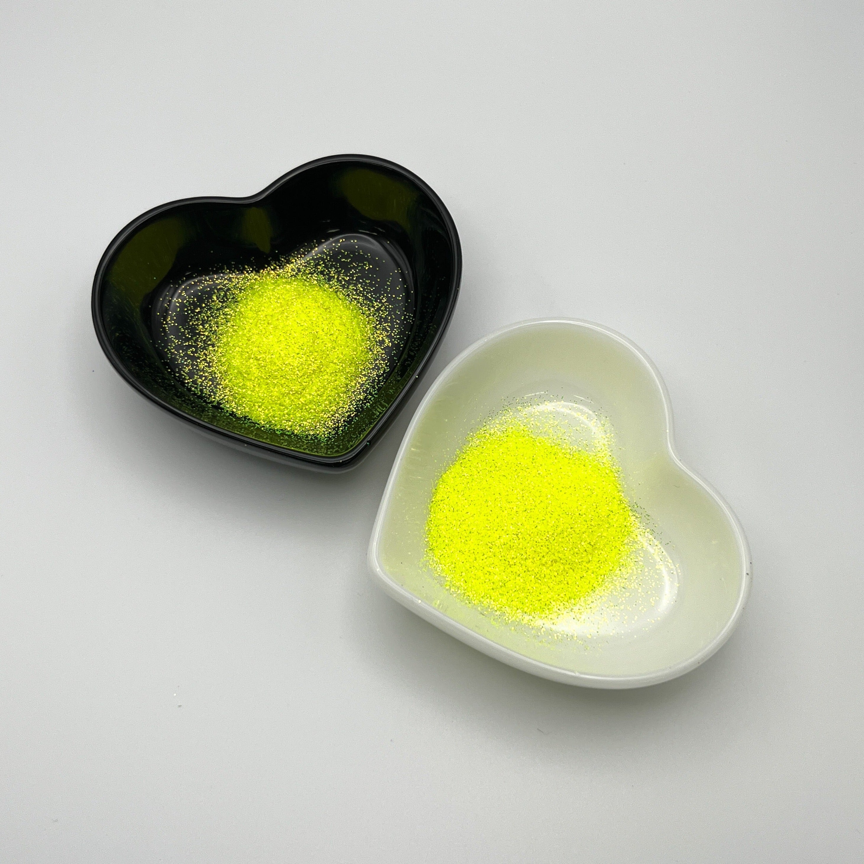 Two heart-shaped dishes, one black and one white, both containing yellow extra fine glitter.