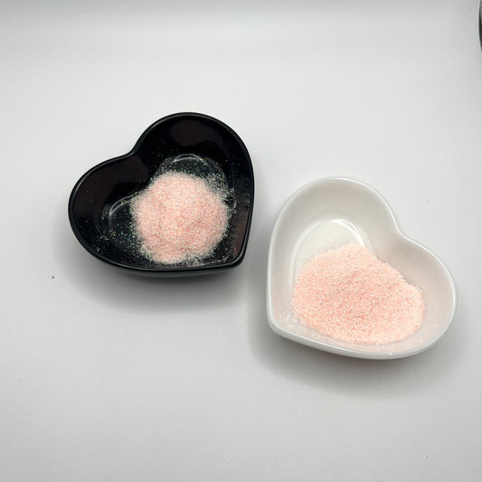 Two heart-shaped dishes, one black and one white, both containing pale pink extra fine glitter.