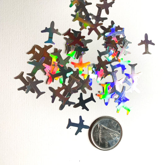 Silver holographic airplane shaped glitter on a white background with a dime used to show size reference. 