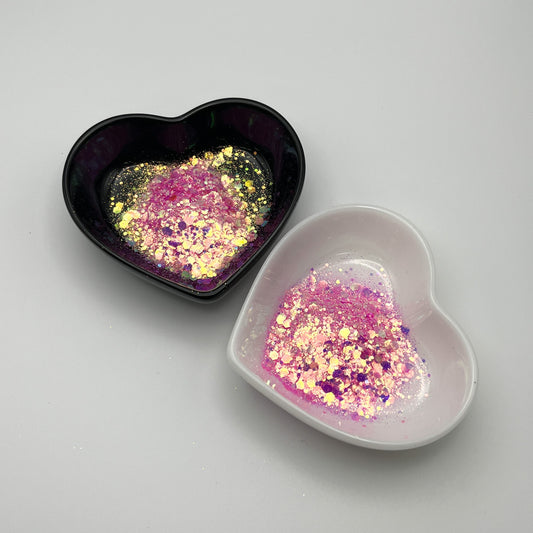 Two heart-shaped dishes, one black and one white, containing light pink chunky glitter mix.