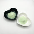 Two heart-shaped dishes, one black and one white, both containing pale green extra fine glitter.