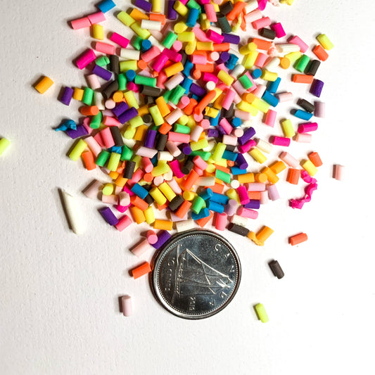 rainbow polymer clay sprinkles on a white background with a dime used to show size reference. 