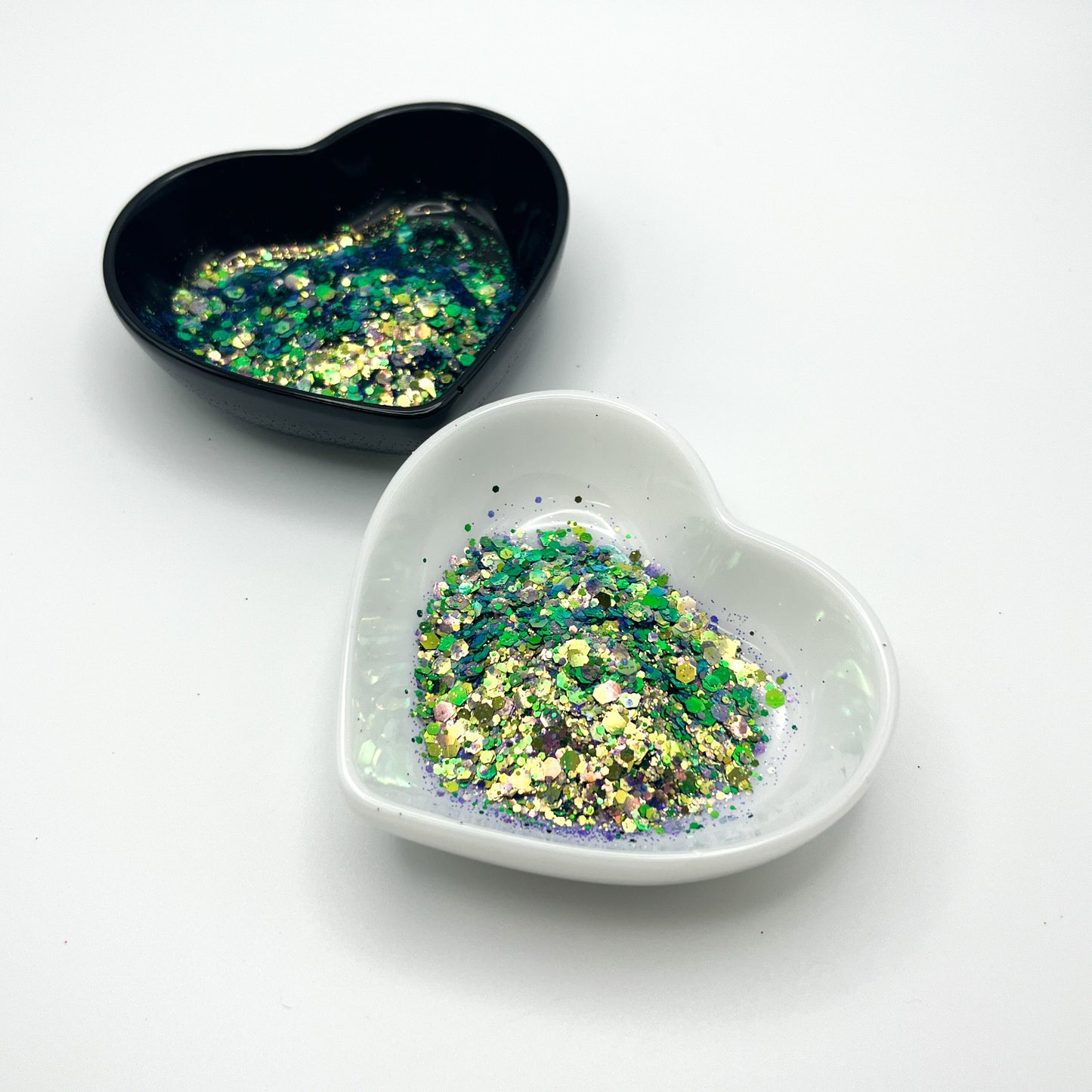 Two heart shaped containers, one black, one white, containing a Purple/Green/Gold chunky glitter mix.
