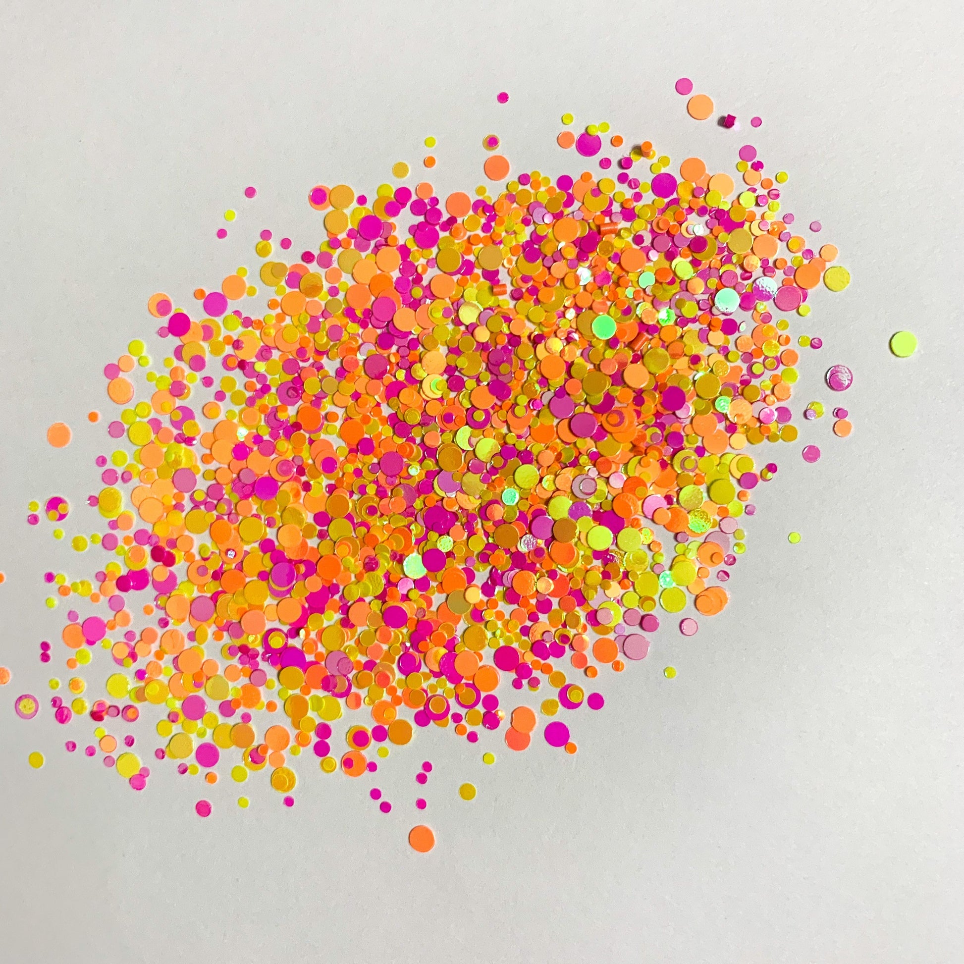 A colorful mix of chunky glitter in orange, pink, yellow, and other colors spread on a white background.