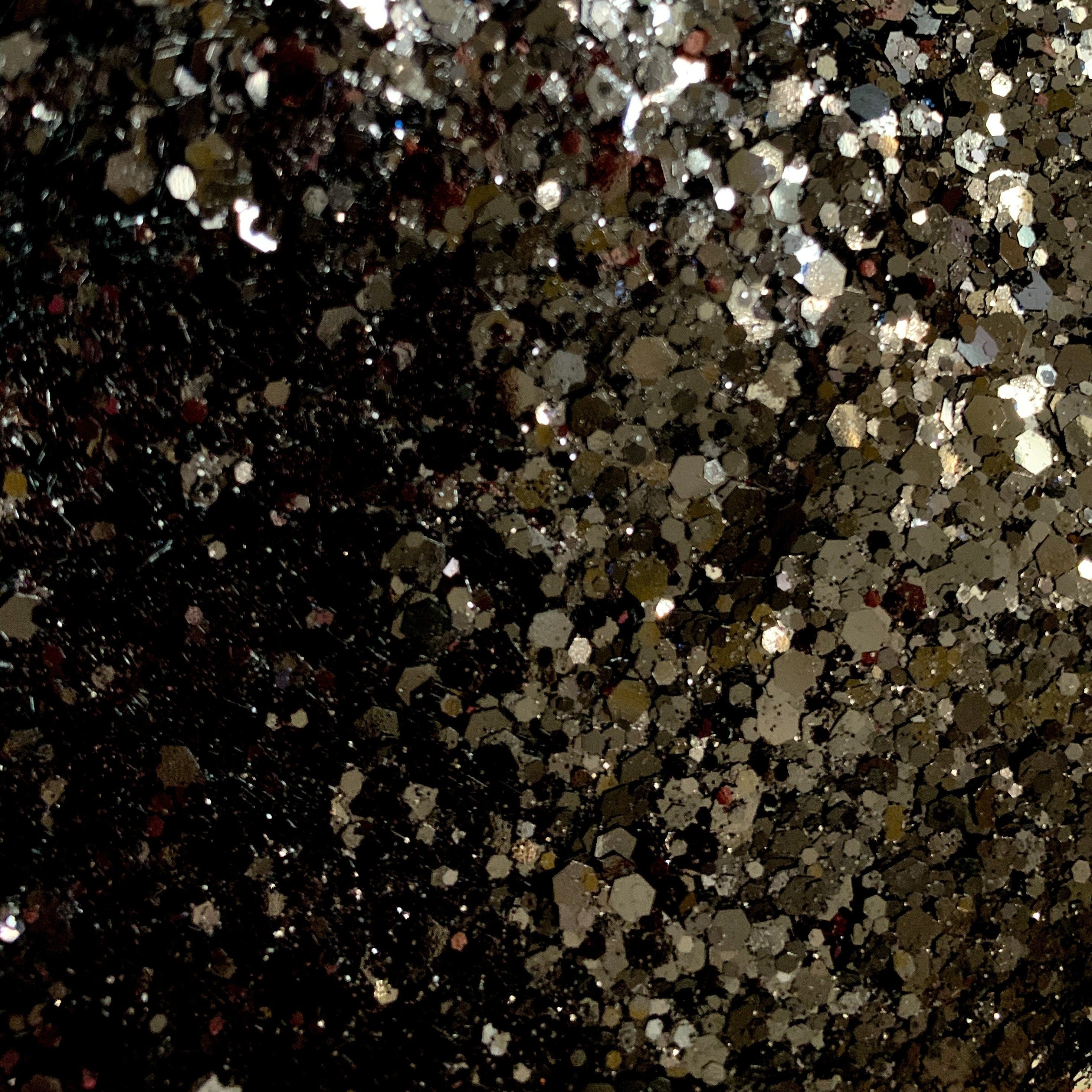 A close-up image of black polyester glitter with various sizes reflecting light, creating a shiny and sparkling appearance.