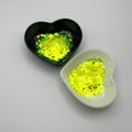 Two heart-shaped dishes containing yellow chunky glitter, one black dish and one white dish.