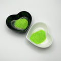 Two heart-shaped dishes, one black and one white, both containing green extra fine glitter.
