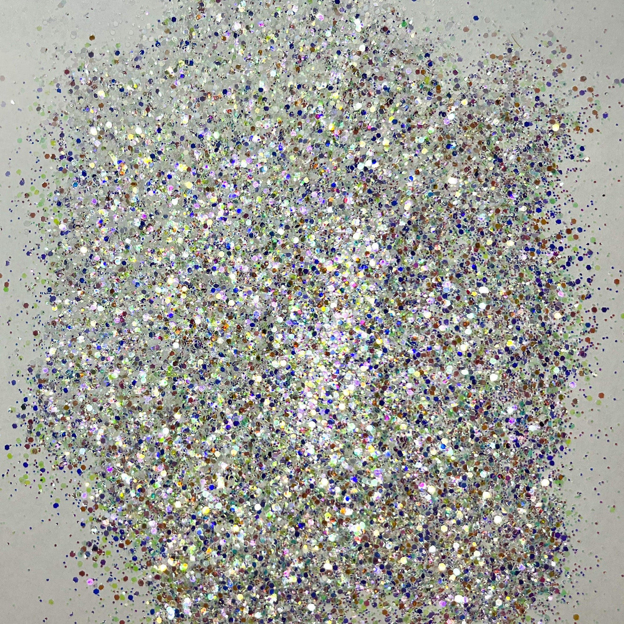 A pile of multicolored glitter, with a predominance of white/rainbow hues, spread out on a surface.
