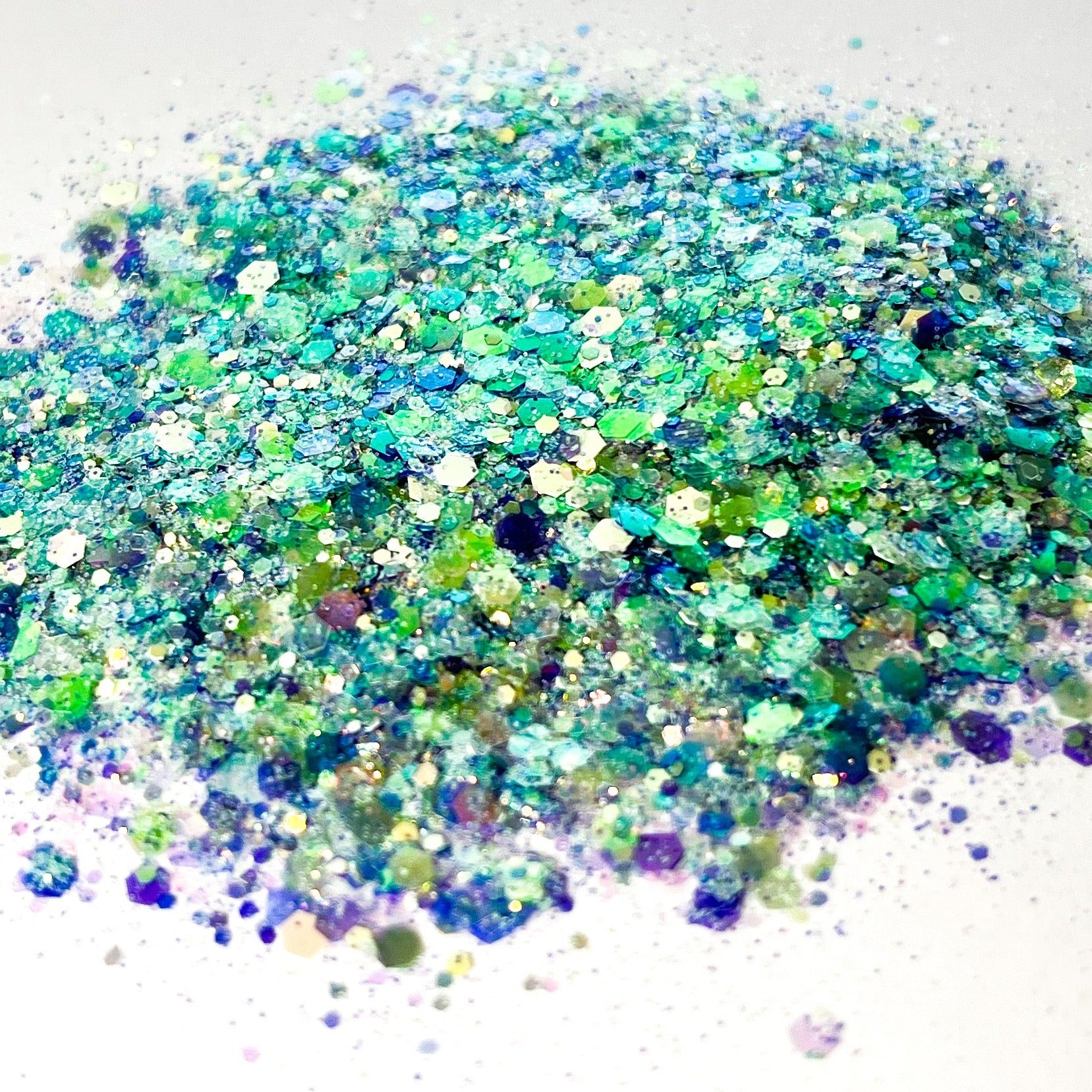 A pile of mixed colours of chunky glitter, including White/Green/Mint/Purple/Blue on a white background.