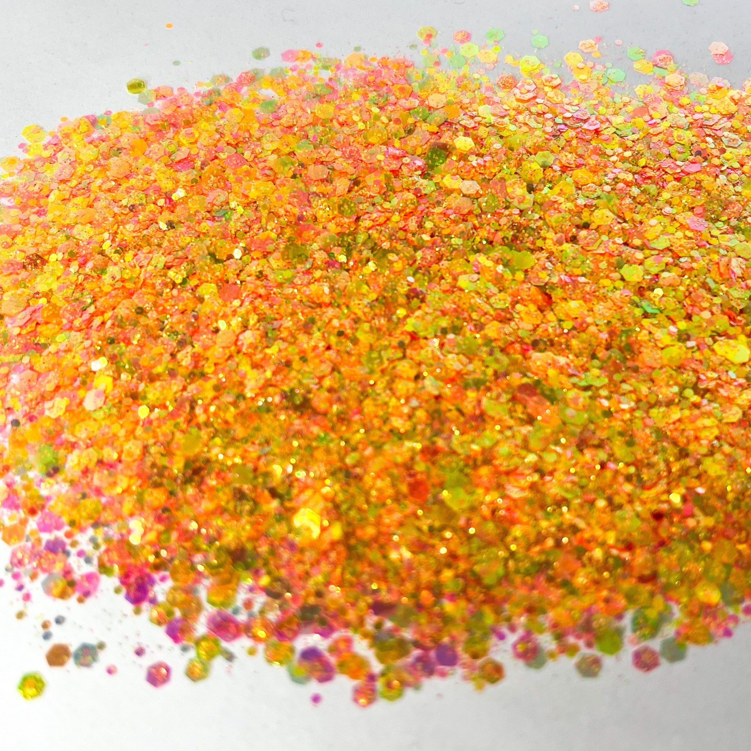 A pile of mixed colours of chunky glitter, including Orange/Pink/Green/Coral on a white background.