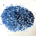 A pile of denim blue chunky glitter on a white background.
