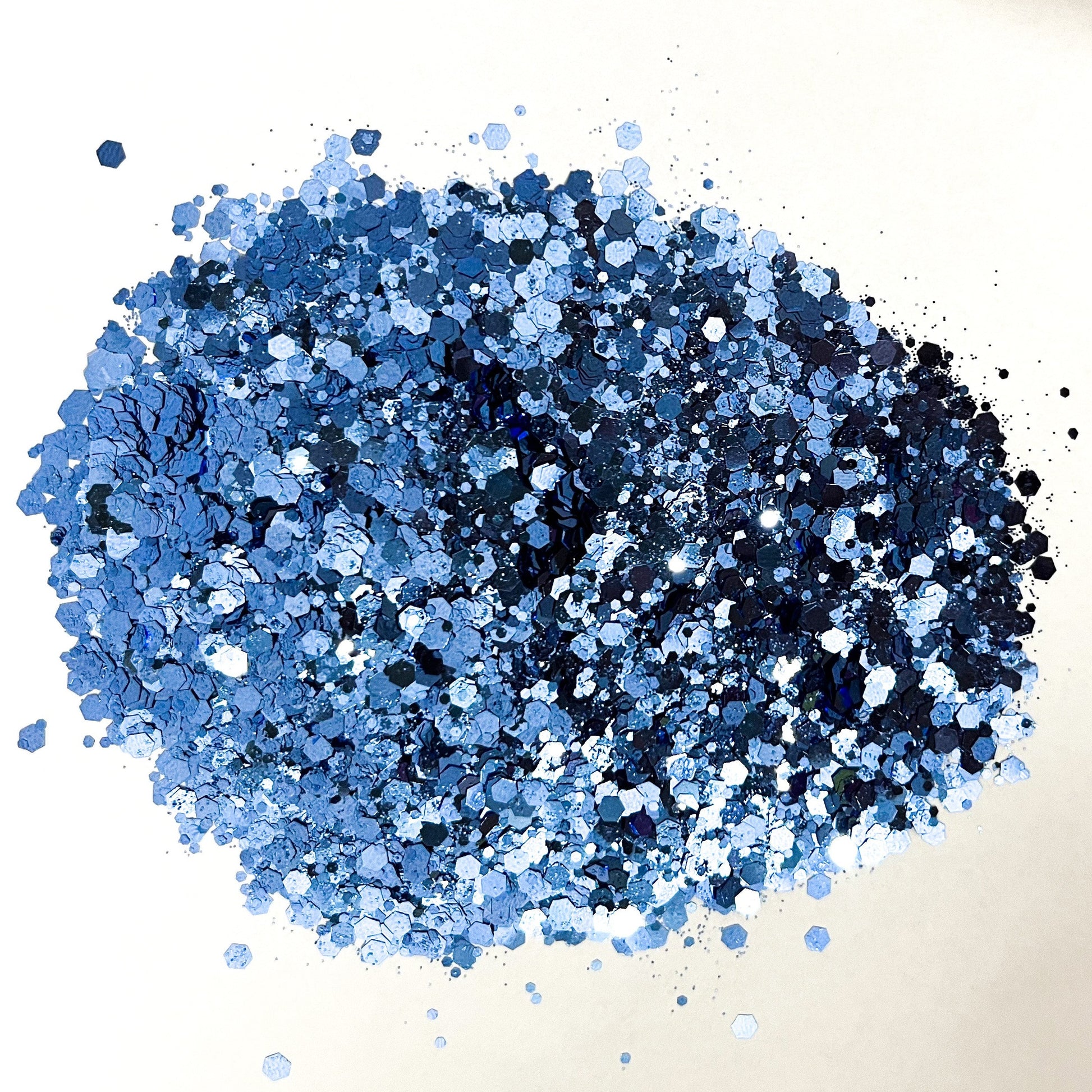 A pile of denim blue chunky glitter on a white background.