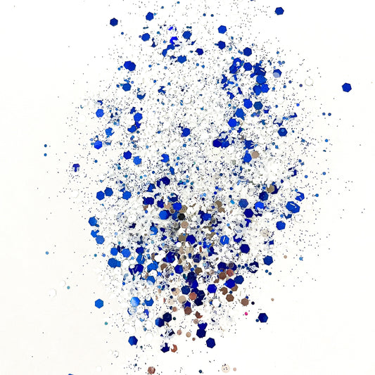 A mixture of blue, white, and silver chunky glitter spread out on a white background, resembling snowflakes.