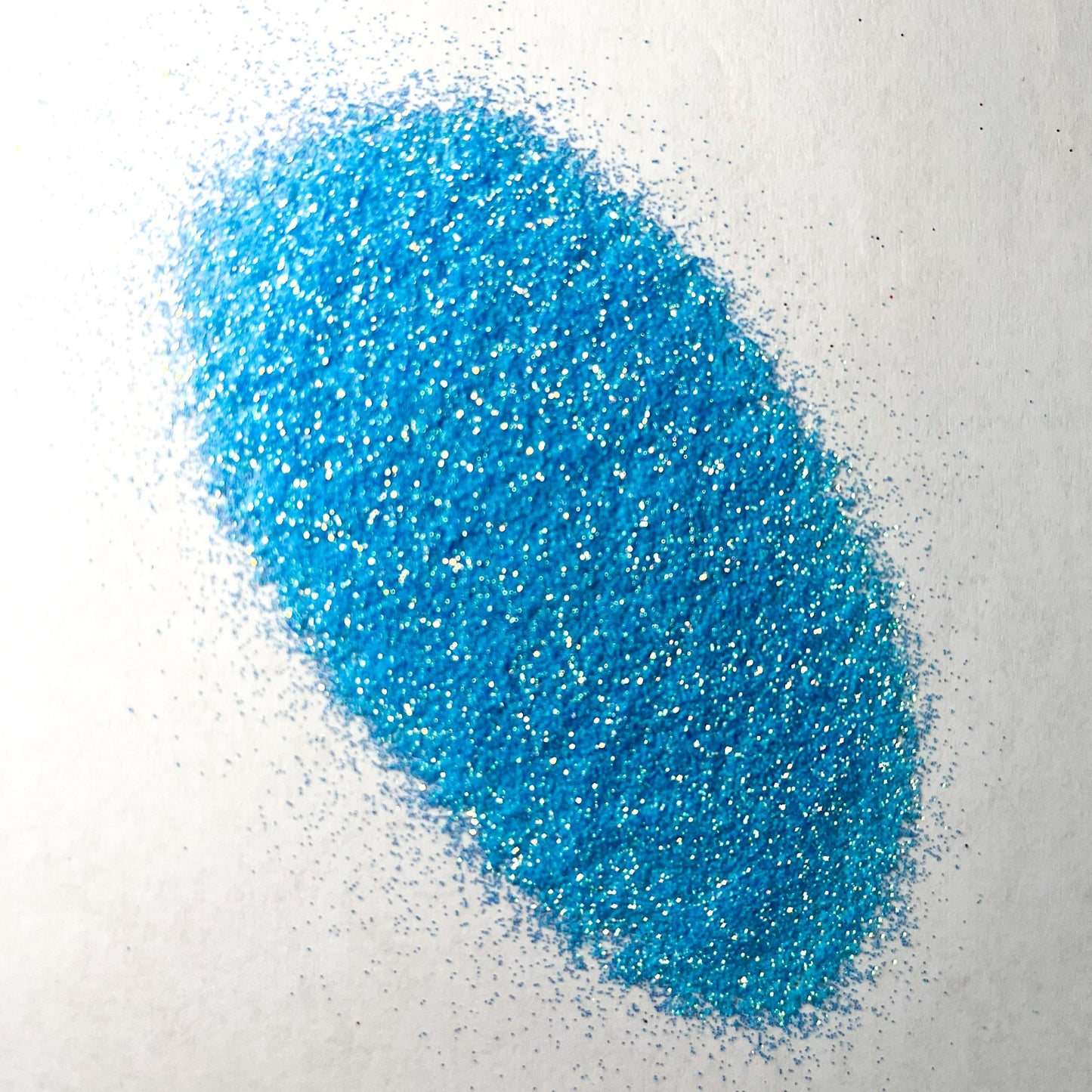 A pile of blue extra fine iridescent glitter spread on a white background.