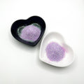 Two heart-shaped dishes, one black and one white, both containing light purple extra fine glitter.