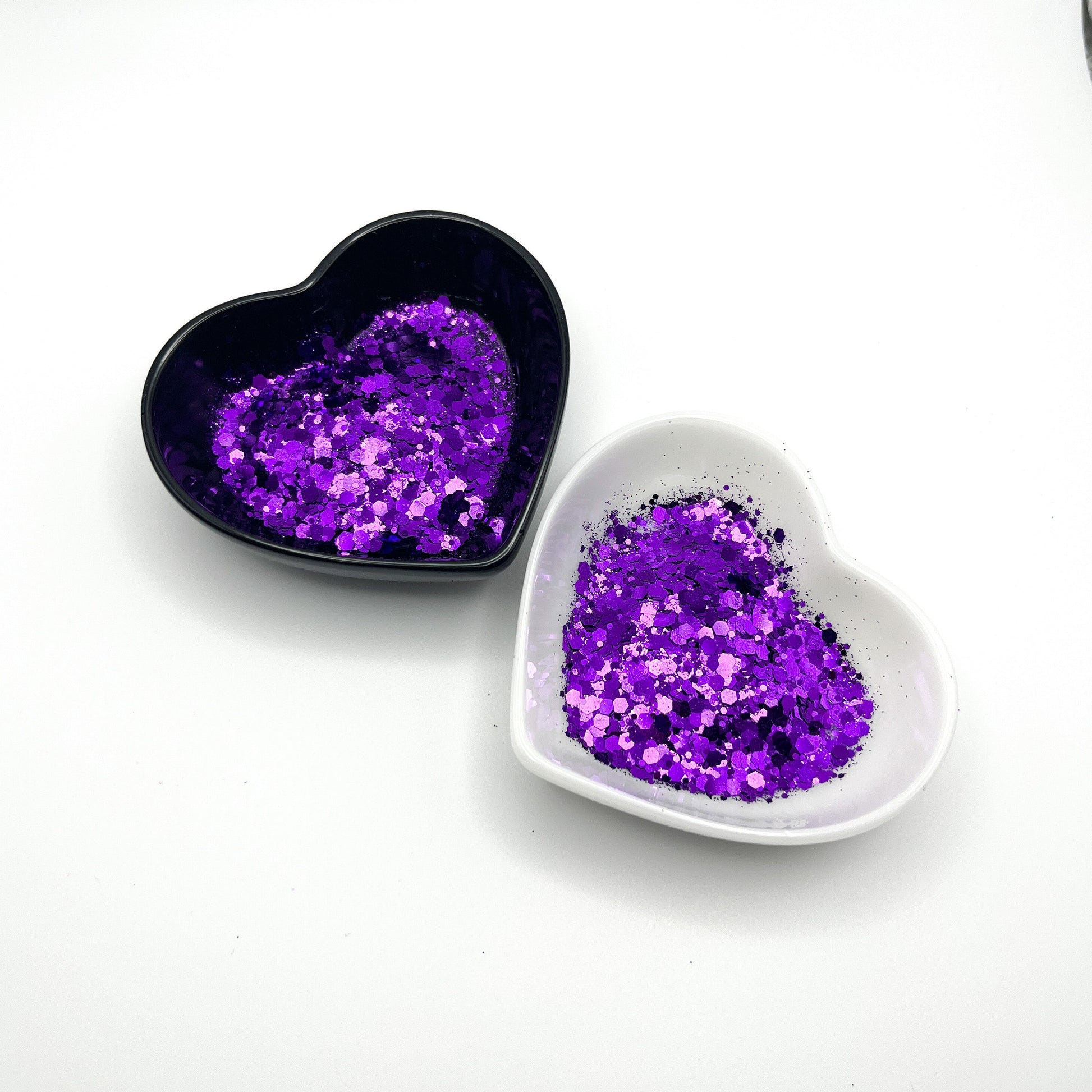 Two heart shaped containers, one black, one white, containing a Purple chunky glitter mix.