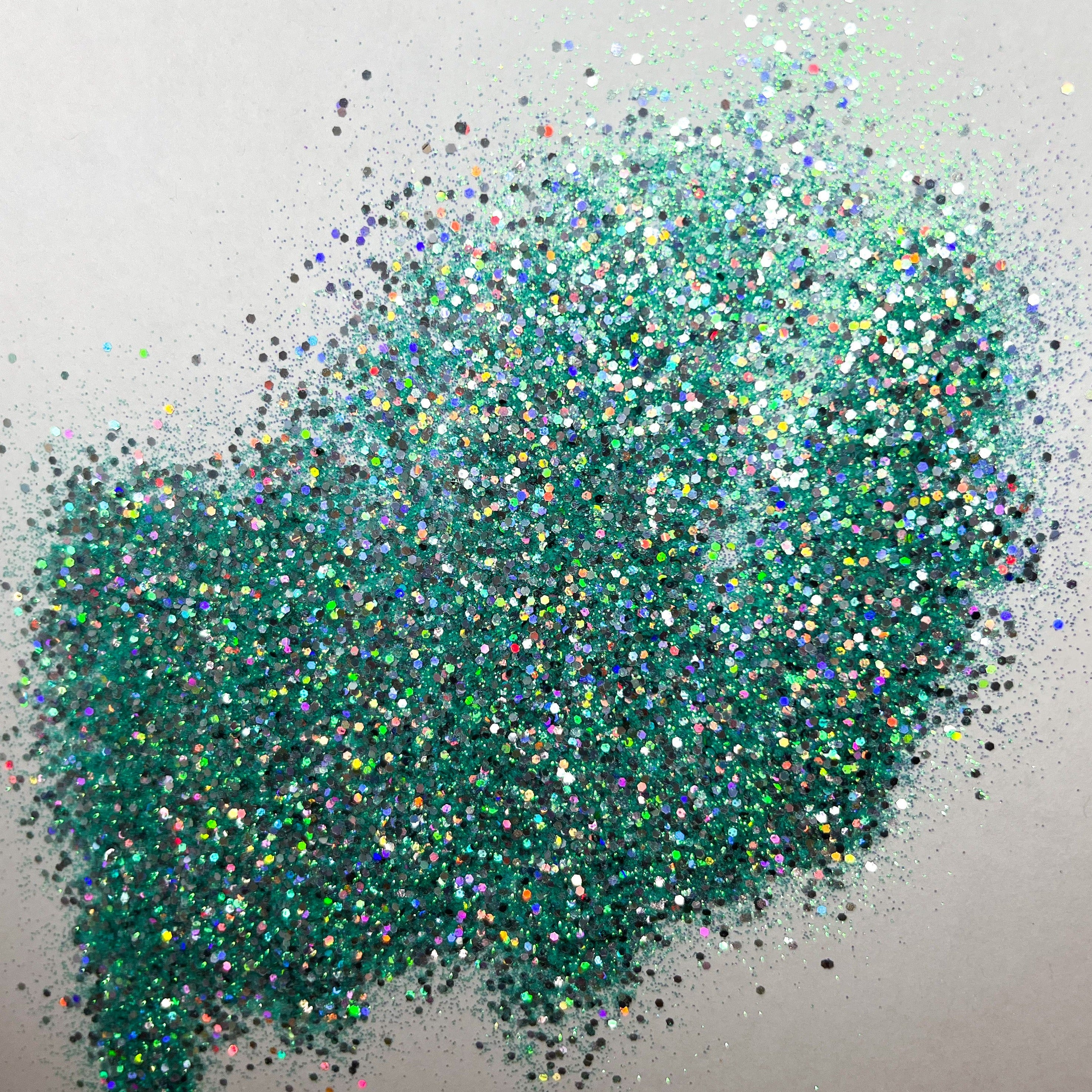 A pile of multicolored glitter, with a predominance of aqua hues, spread out on a surface.