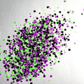A mixture of purple, green, and black glitter circles scattered on a white  surface.