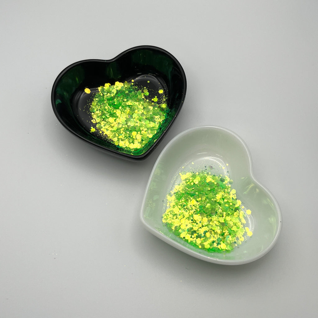 Two heart-shaped dishes, one black and one white, containing green chunky glitter.