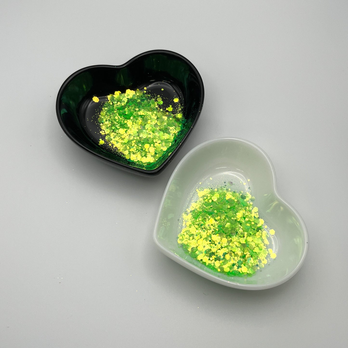 Two heart-shaped dishes, one black and one white, containing green chunky glitter.
