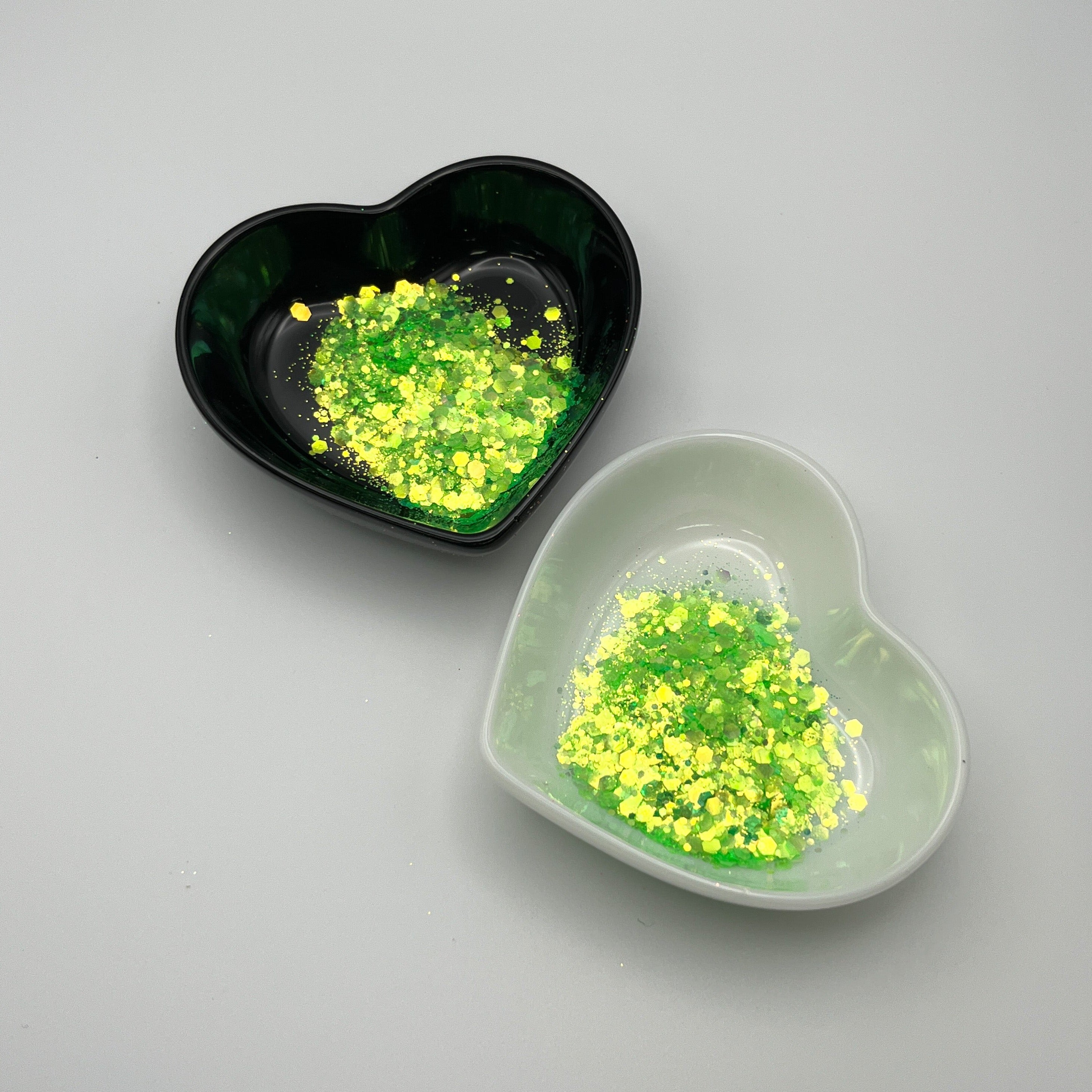 Two heart-shaped dishes, one black and one white, containing green chunky glitter.