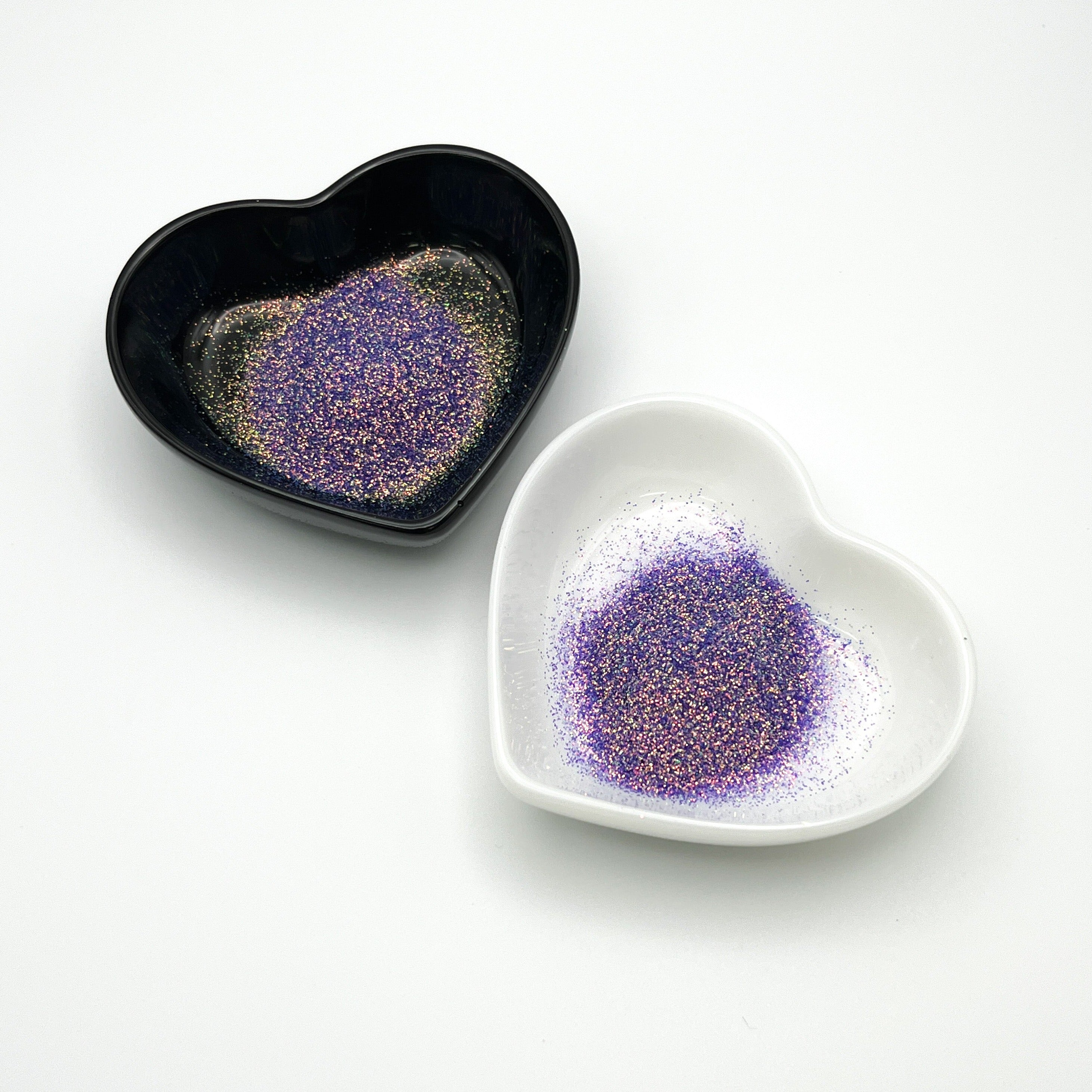 Two heart-shaped dishes, one black and one white, both containing purple extra fine glitter.