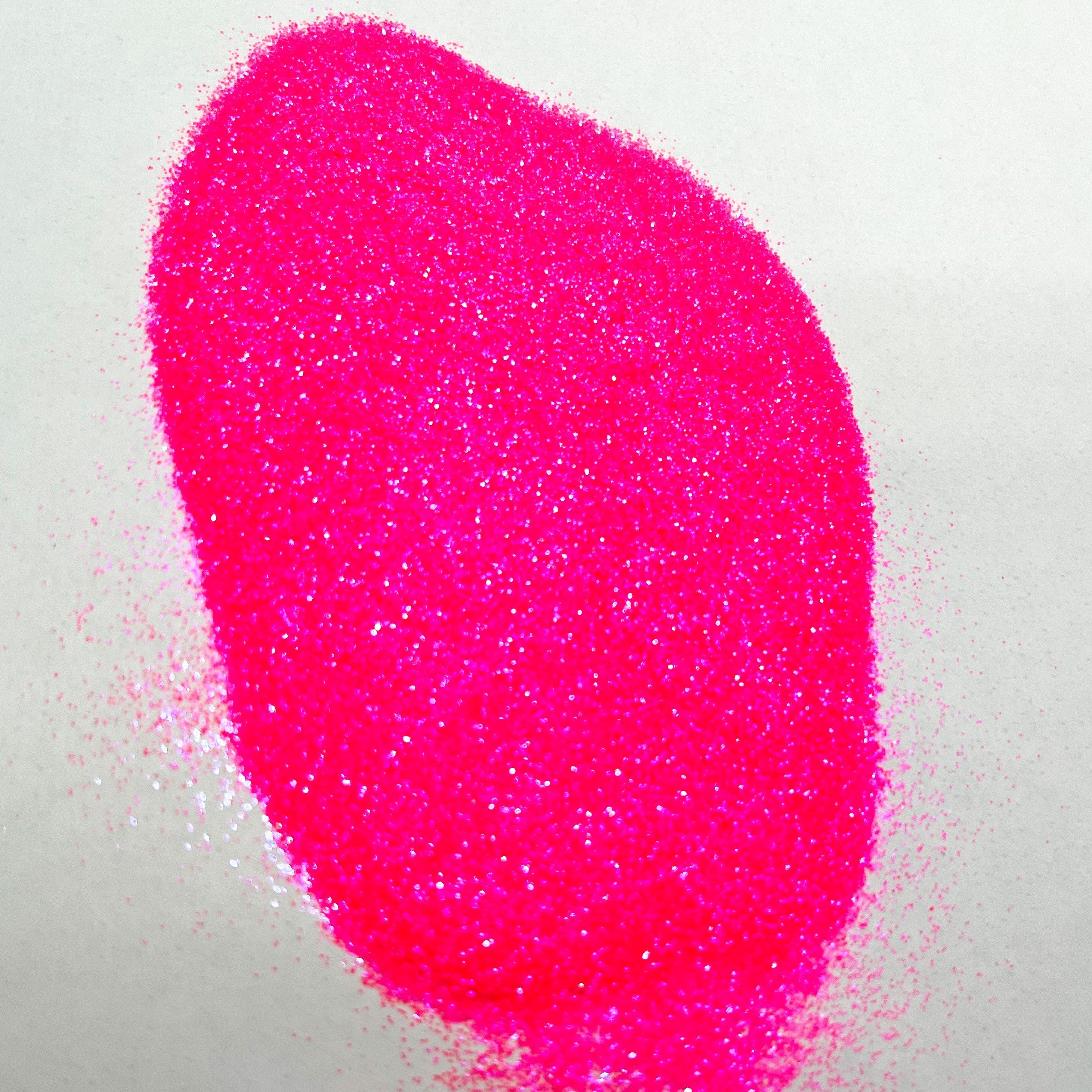 A pile of hot pink, extra fine, iridescent glitter spread on a white surface.
