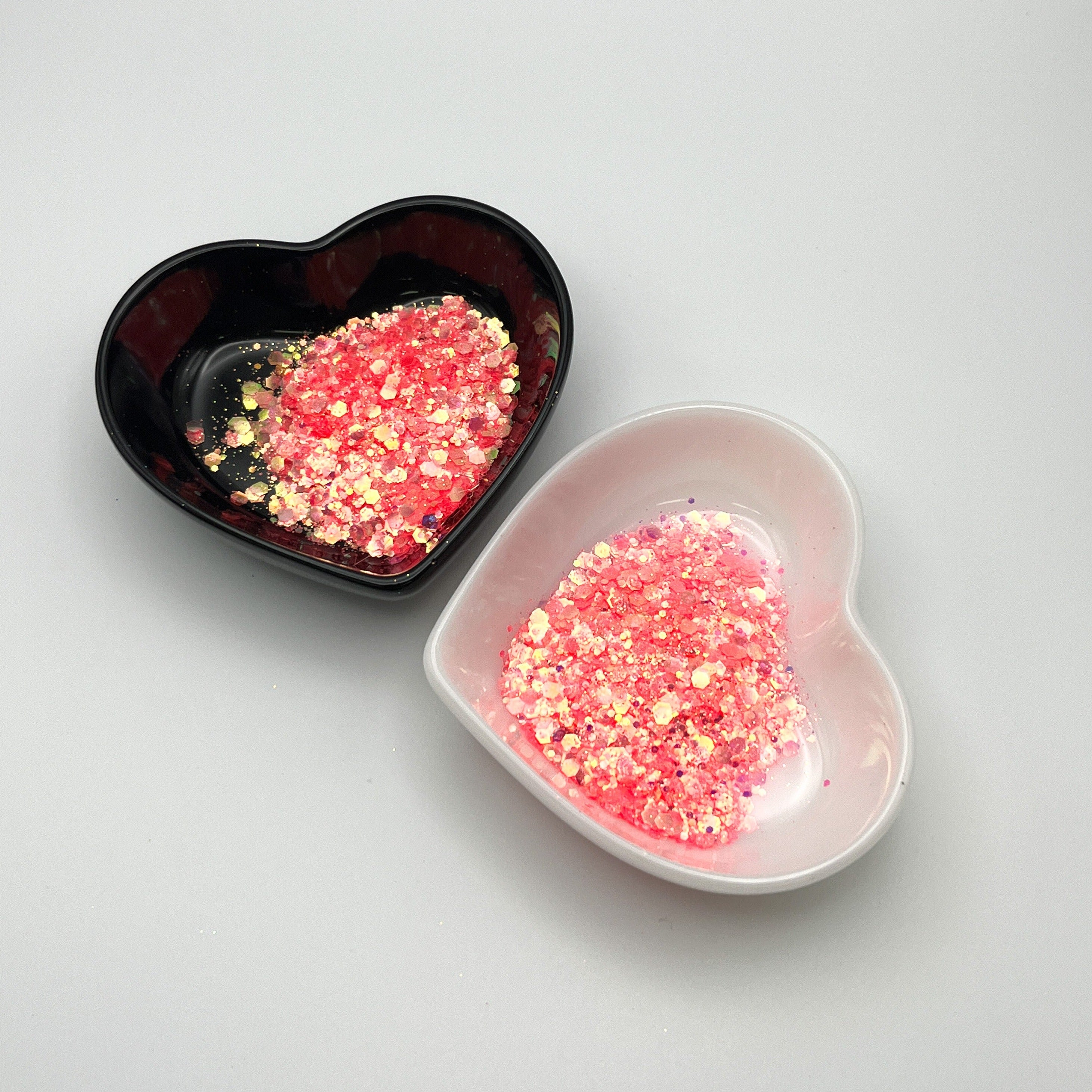 Two heart-shaped dishes, one black and one white, containing pink chunky glitter.