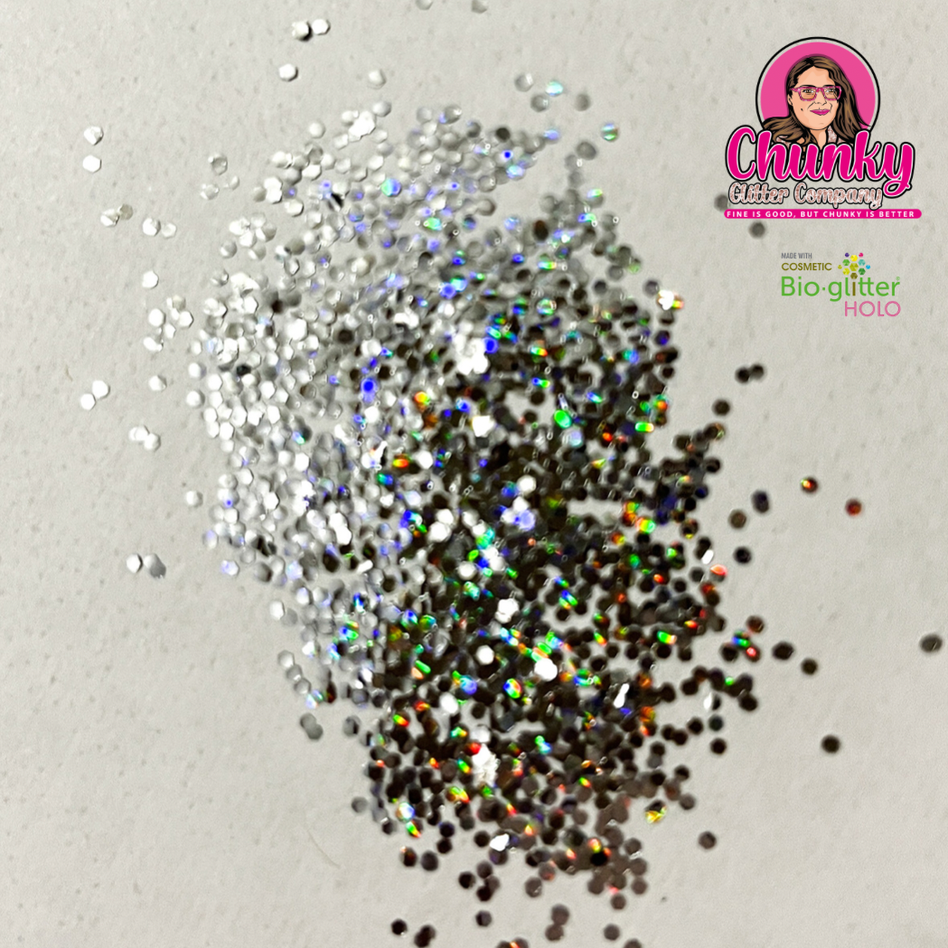 A pile of silver holographic biodegradable glitter on a white surface with a logo in the corner.