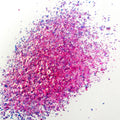 A pile of pink irregular glitter flakes spread out on a white background.