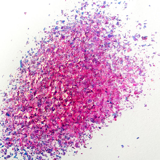 A pile of pink irregular glitter flakes spread out on a white background.