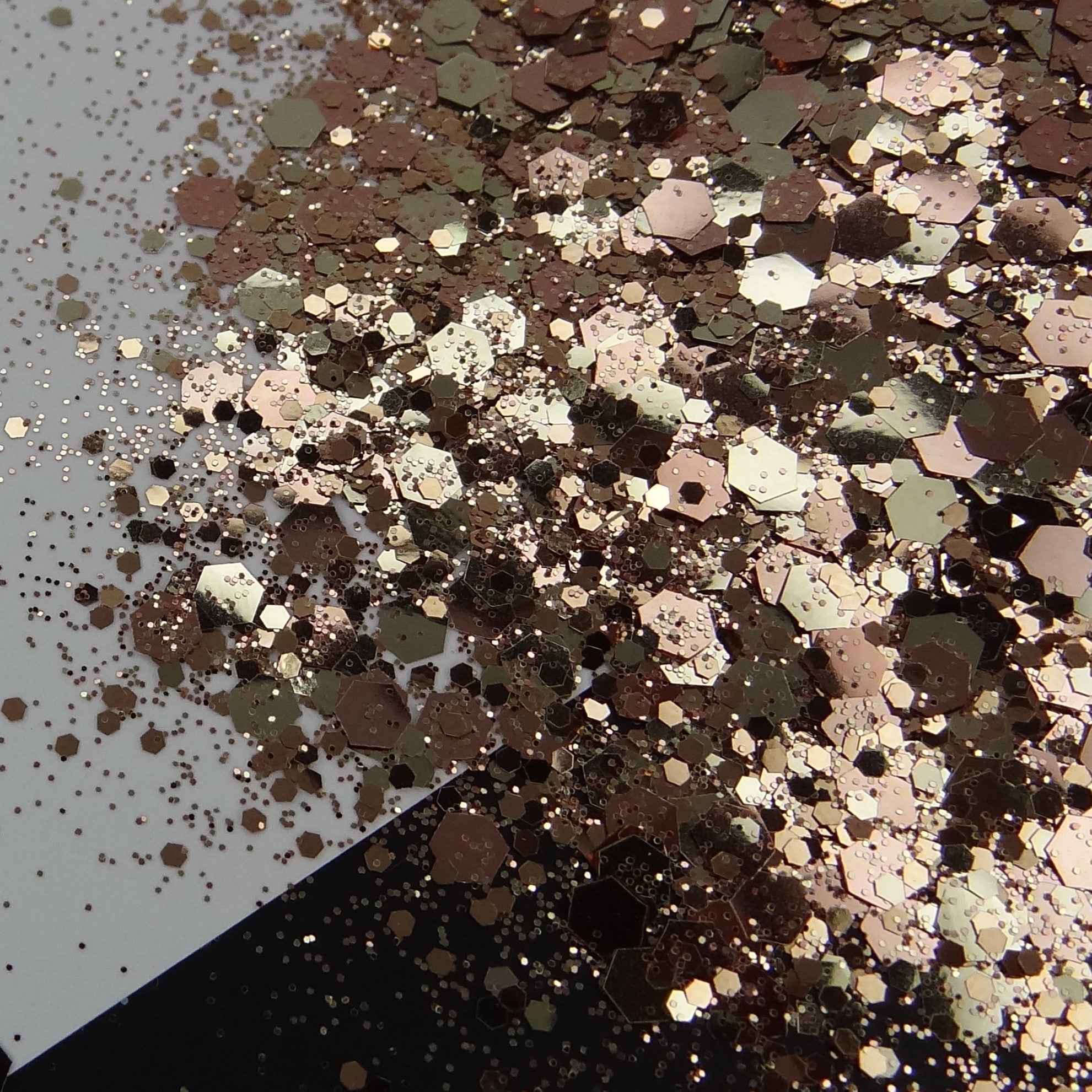 A rose gold and bronze chunky glitter mix spread out on a black and white background.