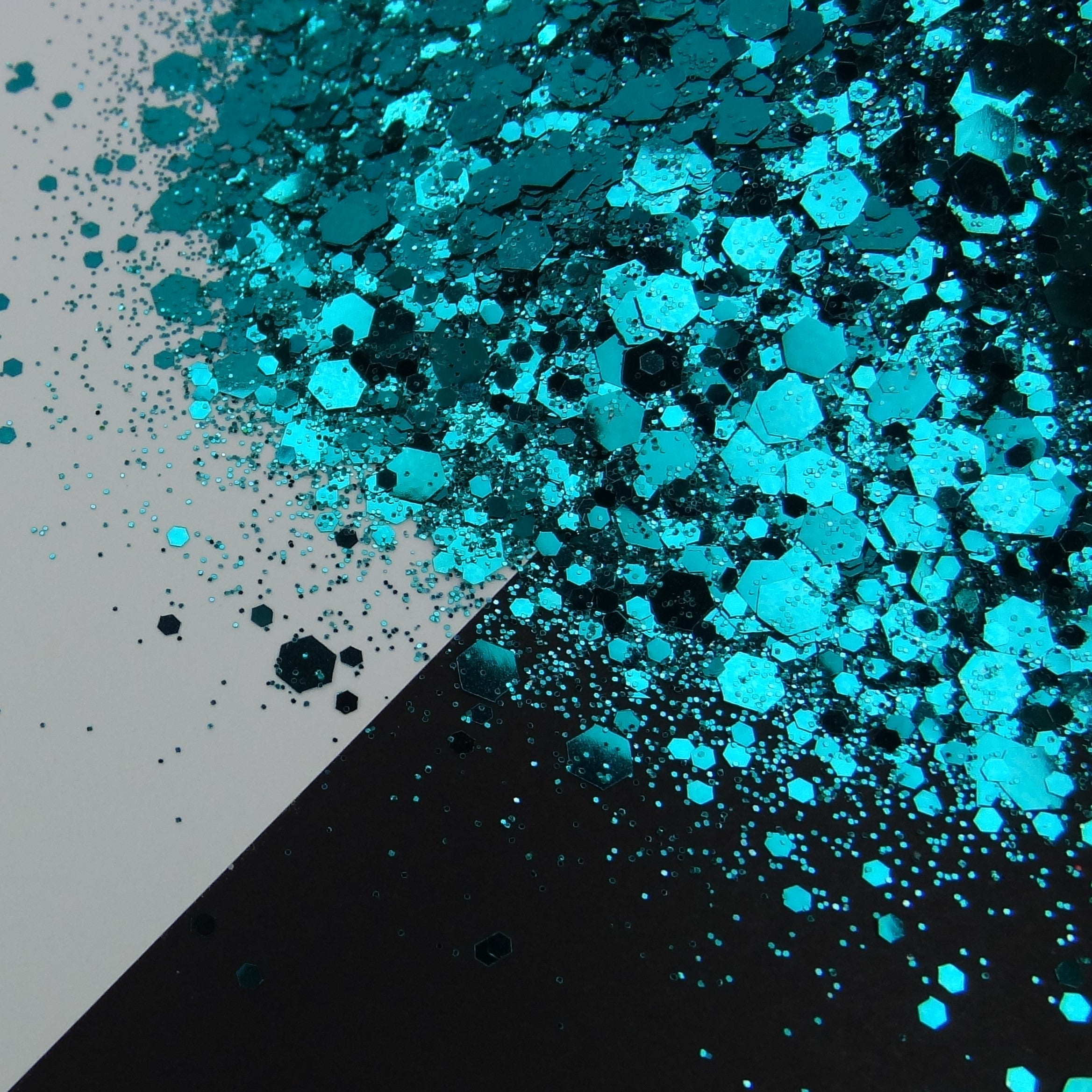 A pile of dark teal chunky glitter on a black and white background.