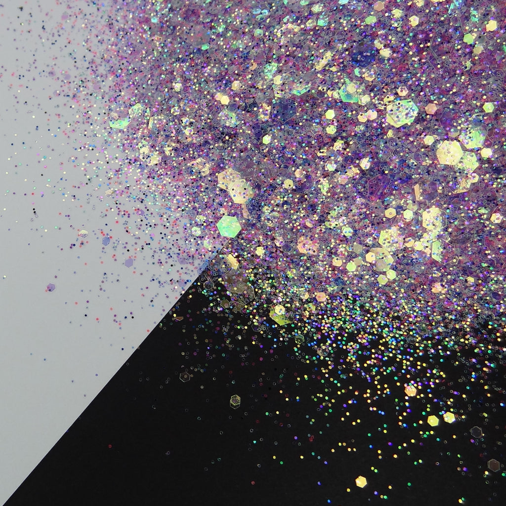 A pile of mixed colours of chunky glitter, including White/Aqua/Purple/Blue/Pink/Navy  on a white and black background.